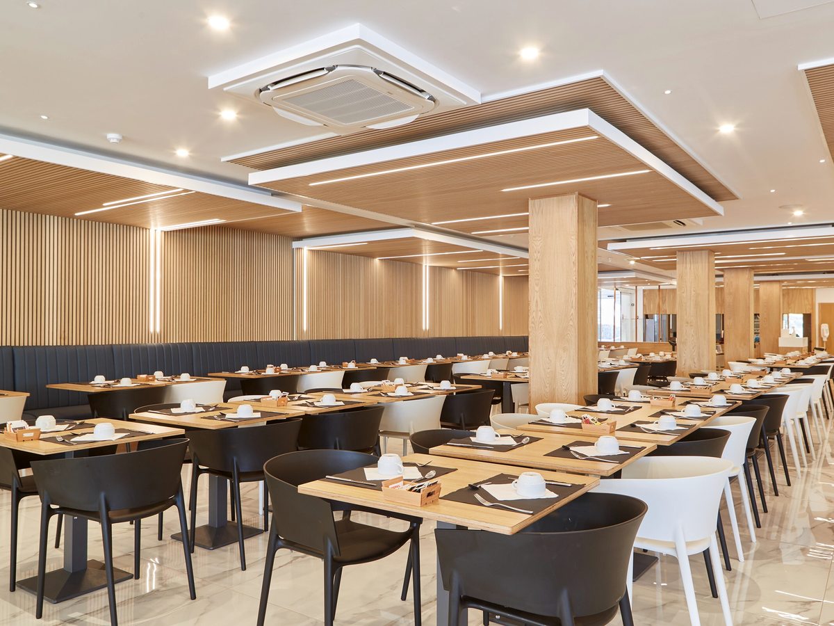 A bright buffet dining room lined with set tables under a wood-panelled ceiling.