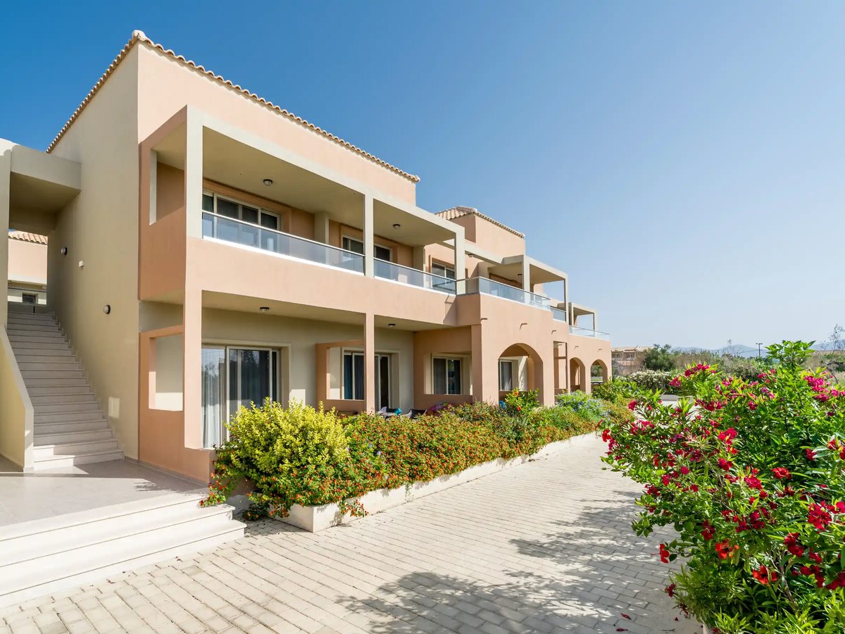 A two-storey accommodation building with balconies in shades of cream and peach, among landscaped shrubs.