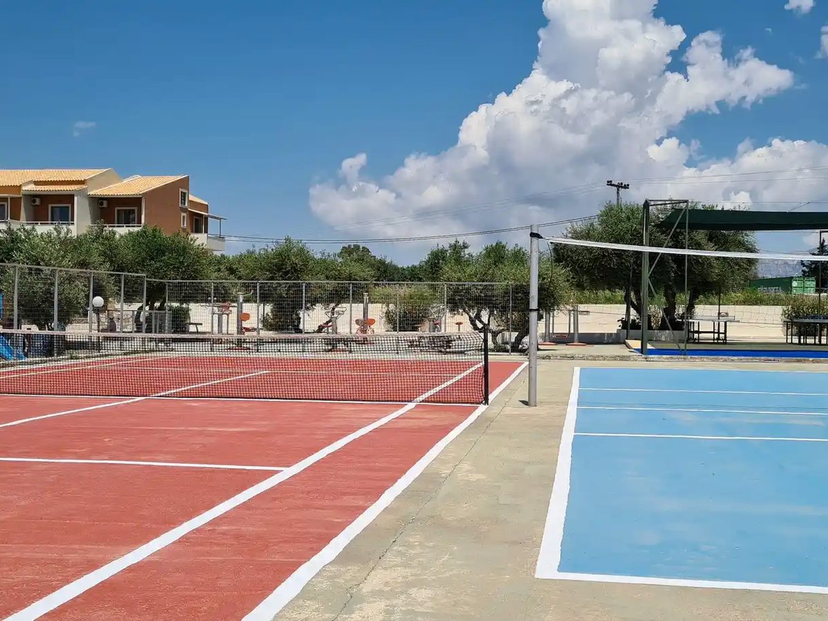 Outdoor multi-sport courts with tennis and basketball markings, olive trees and open countryside behind.