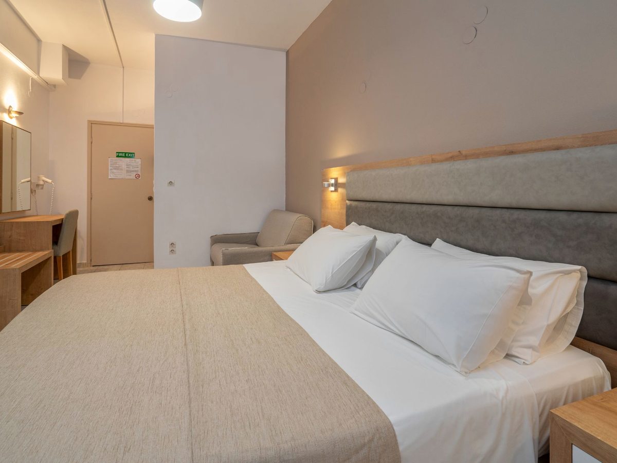 A double bed with a grey upholstered headboard, bedside tables and wall lights in a simply furnished room.