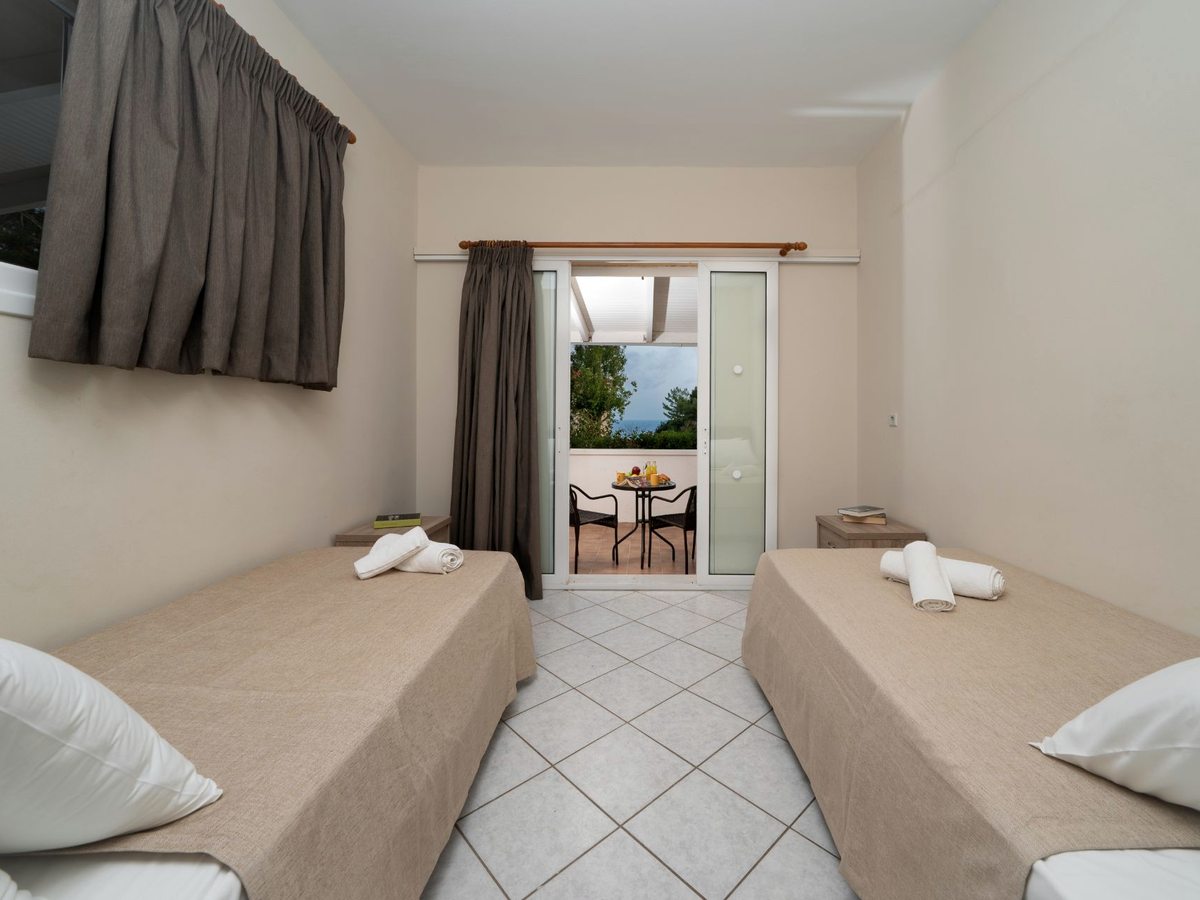A bedroom with two single beds, wooden furniture and a curtained balcony door.