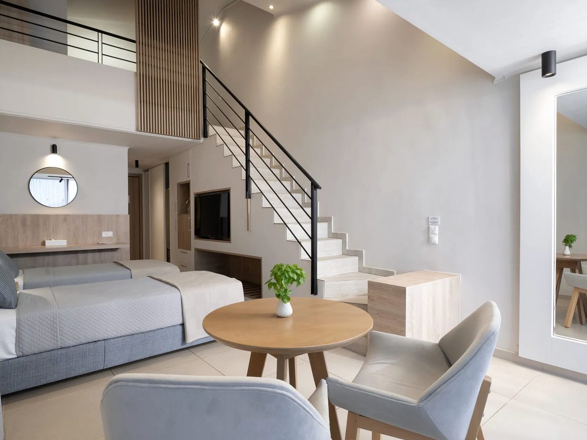 Split-level room with twin beds and a round dining table below and an internal staircase up to a mezzanine.