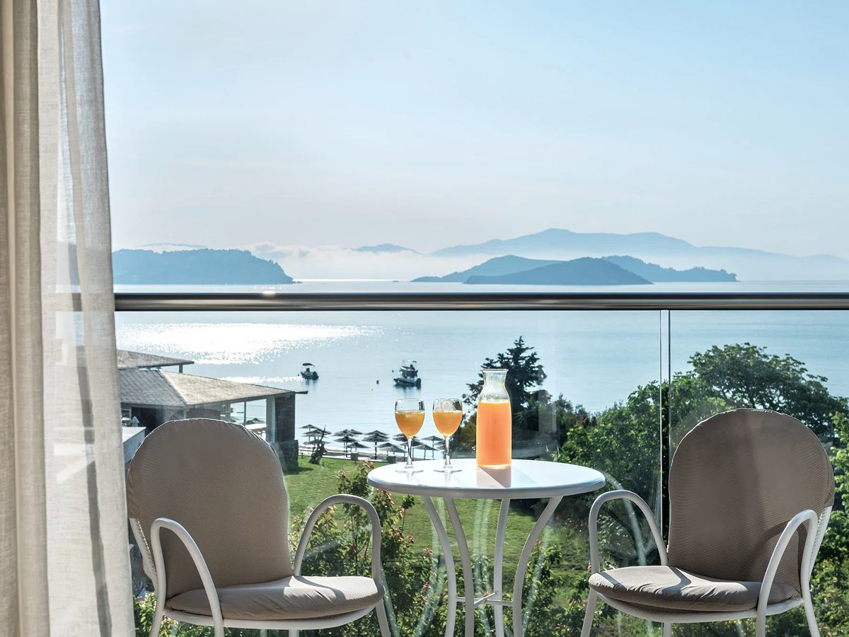 Guest-room balcony with two chairs, a small round table and a glass railing looking out to the sea.