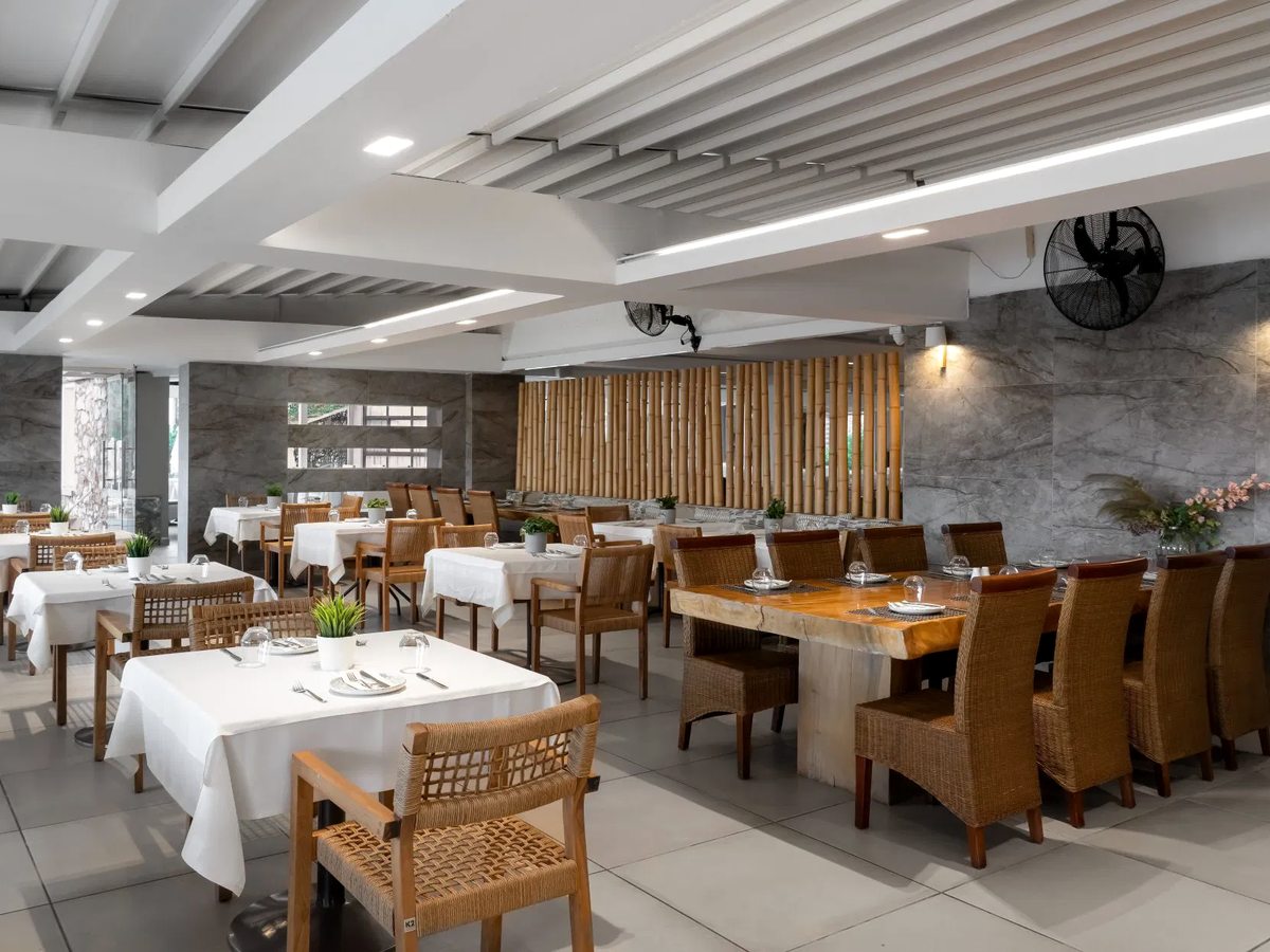 Indoor restaurant with white-clothed tables, wooden chairs and a stone feature wall.
