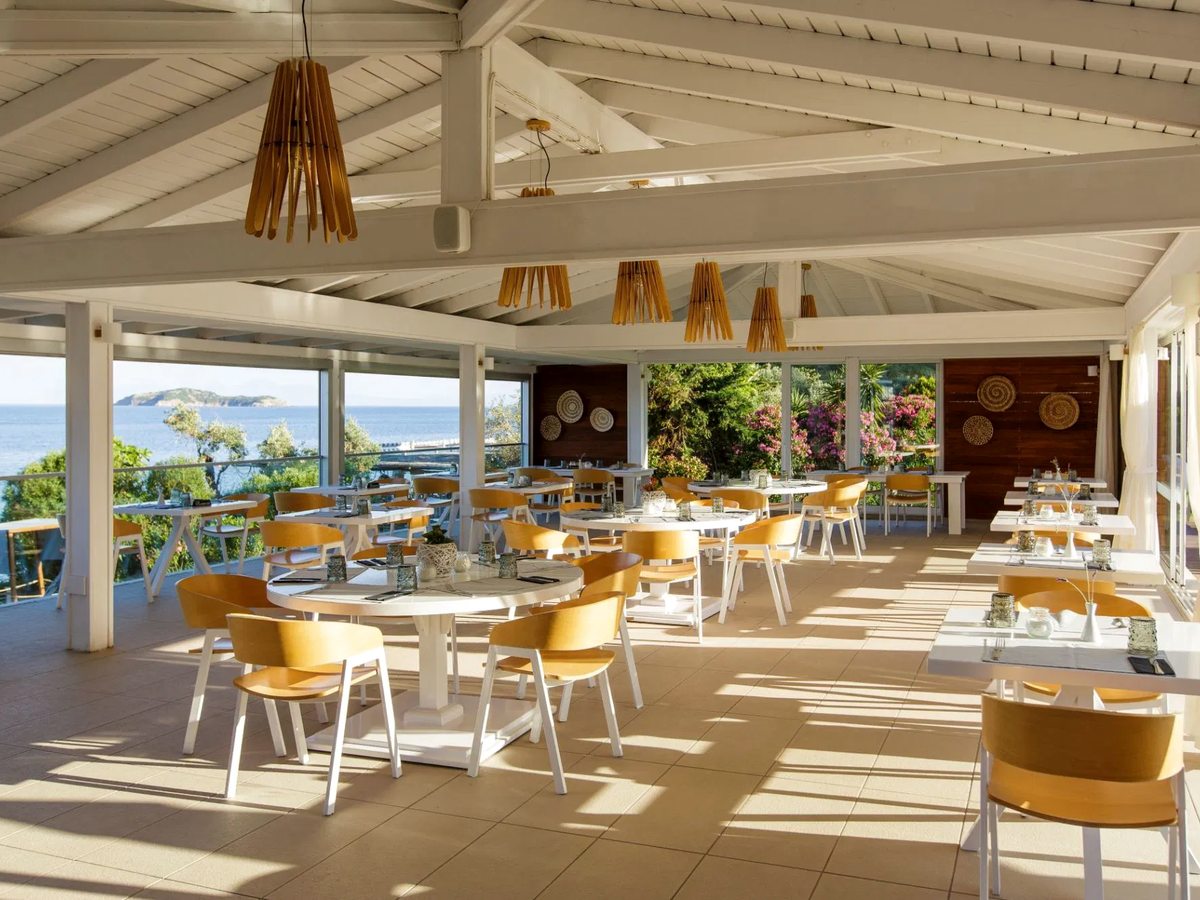 Covered open-air restaurant terrace with white tables and wicker chairs looking out to the sea.