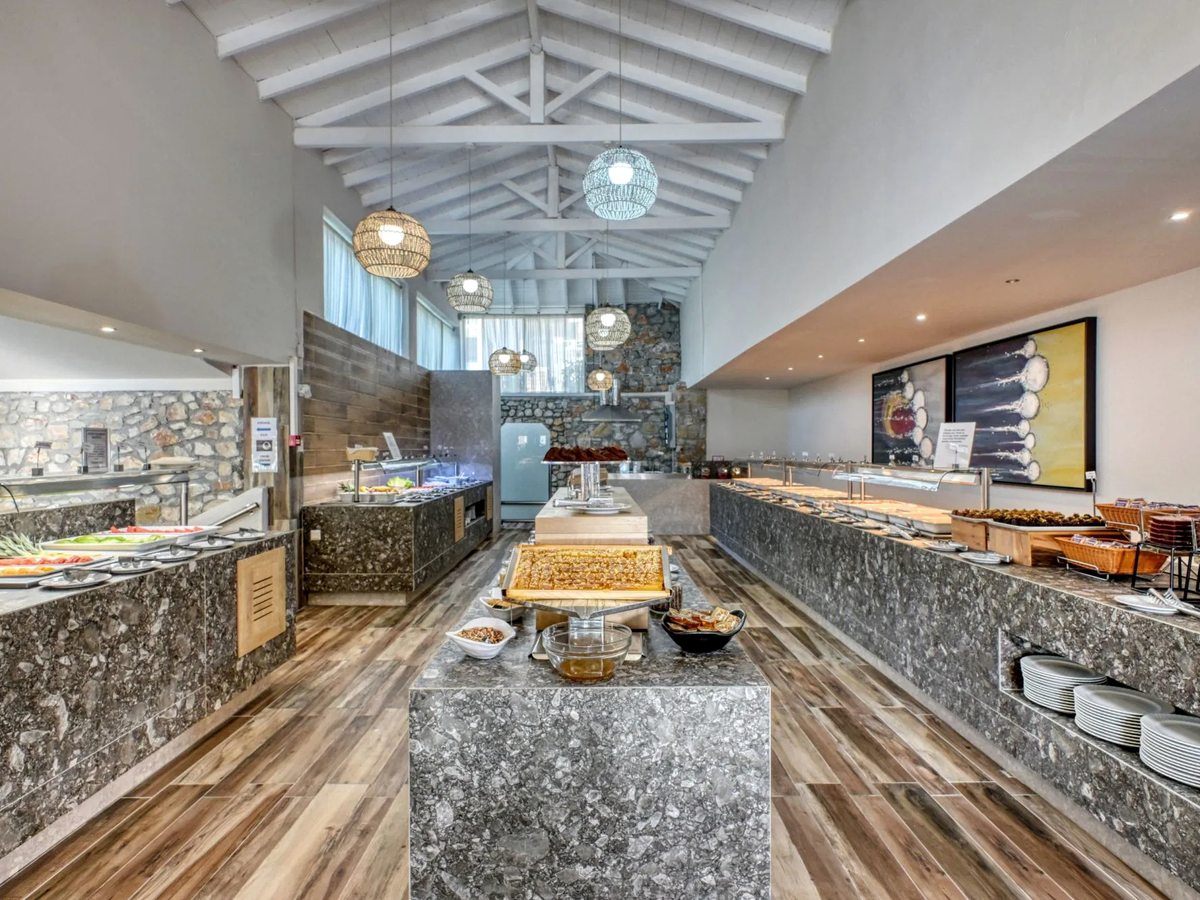 Buffet restaurant with stone-clad counters of hot dishes, breads and salads under pendant lights.