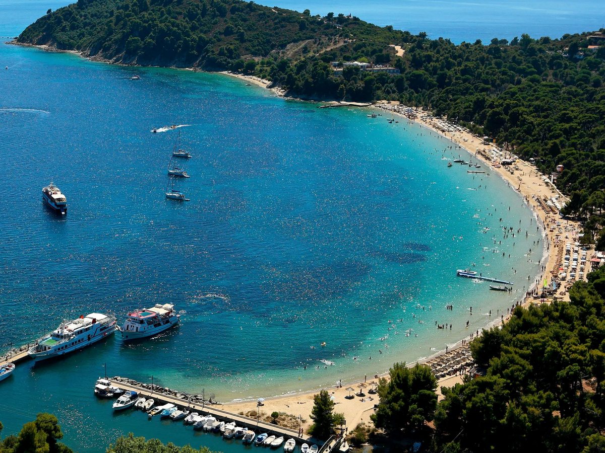 A small harbour with moored boats in a turquoise bay beside a wooded headland.