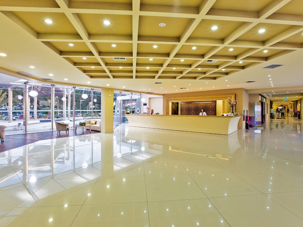 A bright reception hall with a coffered ceiling, a glossy cream floor, a long curved reception desk with staff and a glass frontage onto the gardens.