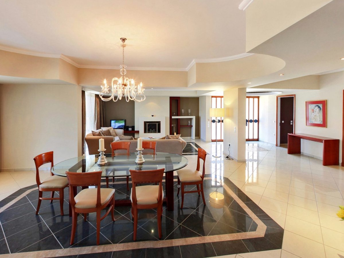 A spacious open-plan suite with a glass dining table and six chairs, a sofa and armchairs around a fireplace and TV, and a polished marble and tiled floor.