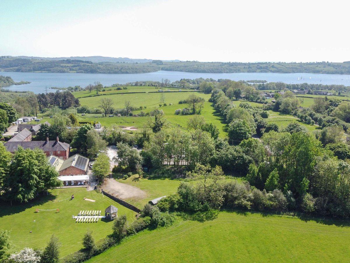 Aerial view over green fields and mature trees to a large reservoir with wooded shores and low hills beyond.
