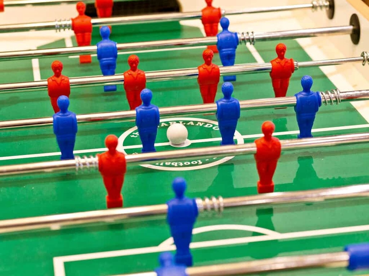 Close view of a table football pitch with rows of red and blue players on steel rods and a white ball at the centre spot.