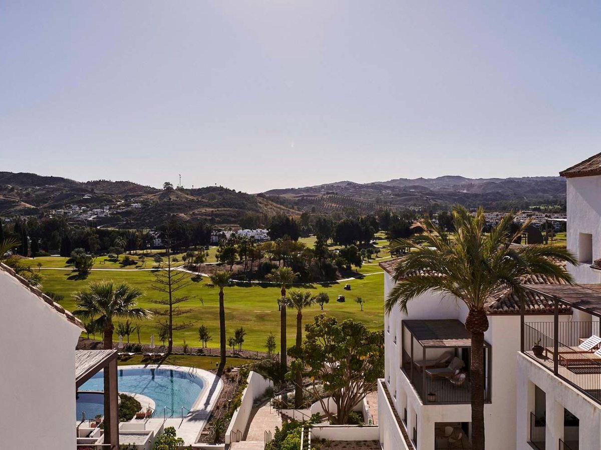 Green golf fairways and palm trees running away to hills and white villages, with hotel buildings and a curved swimming pool in the foreground.