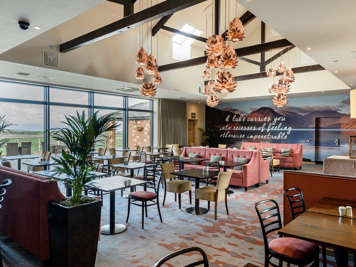 A large restaurant with dining tables, pink and gold banquette seating, copper pendant lights hanging from exposed beams and a lake mural along the far wall.