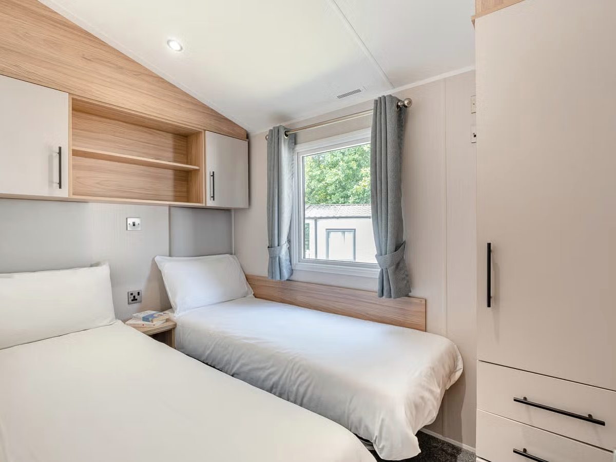 A twin bedroom with two single beds in white bedding, overhead shelving and a tall wardrobe.