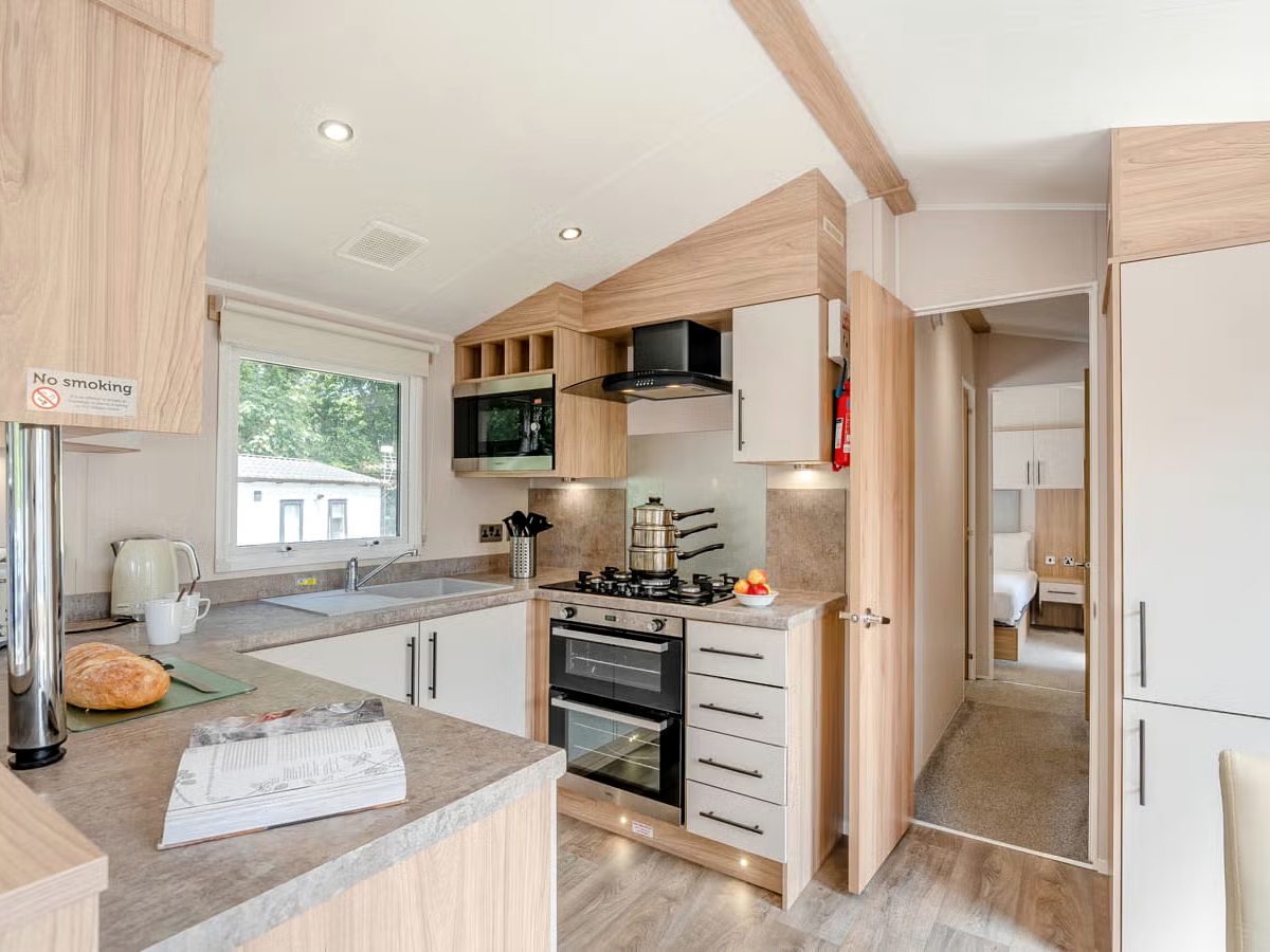 A caravan kitchen with pale cabinets, an oven, gas hob, microwave and a sink under the window.