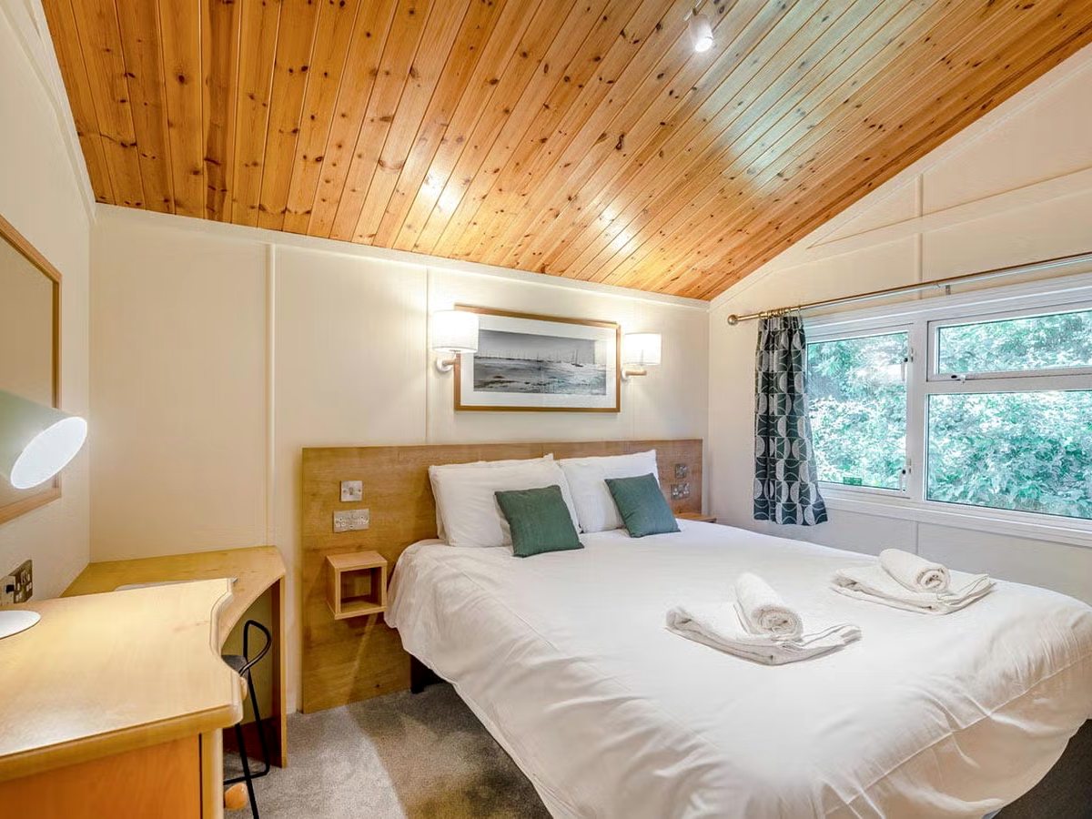 A double bedroom with a wooden headboard, white bedding and folded towels laid on the bed.
