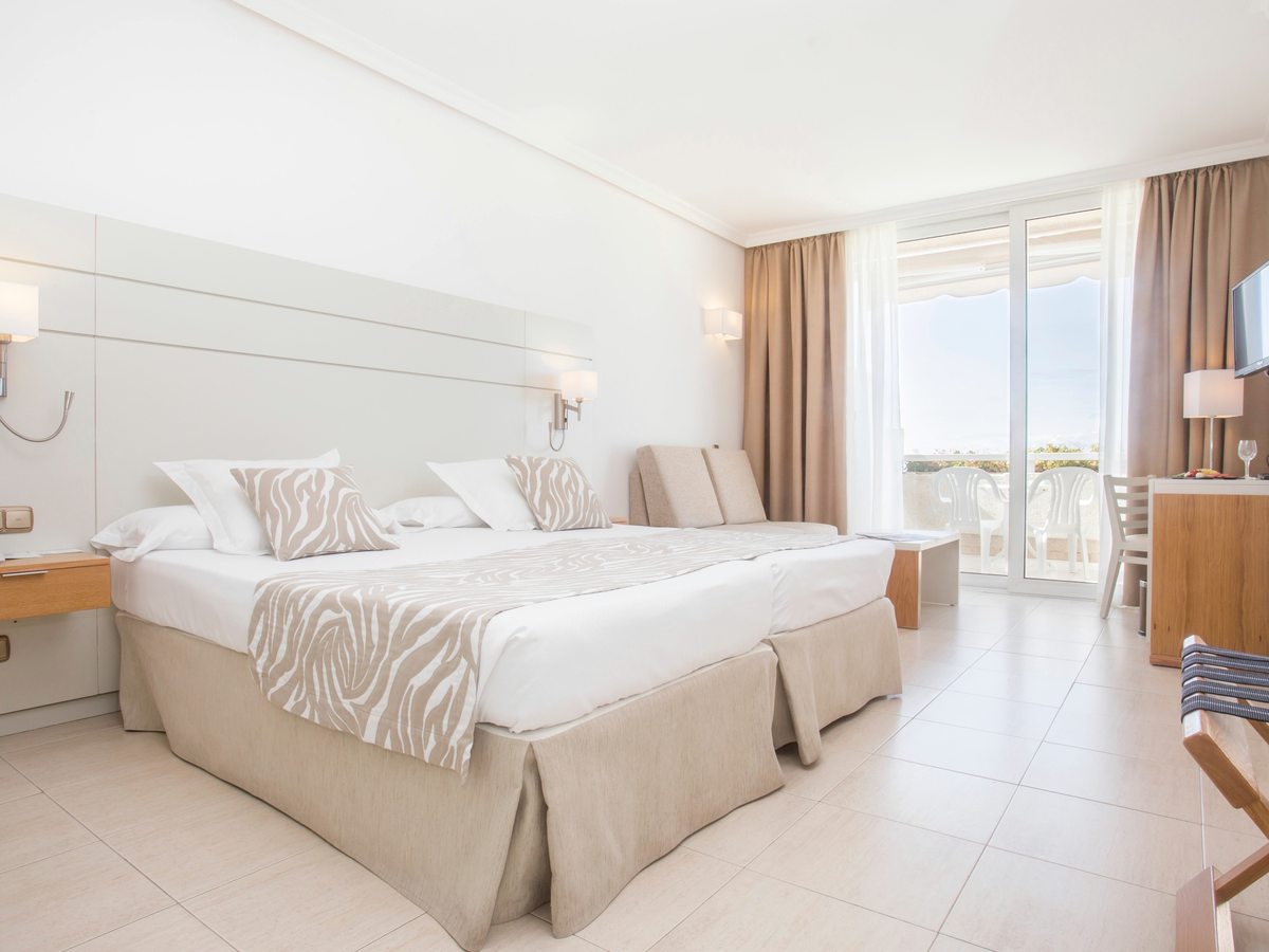 Guest room with twin beds pushed together, a small sofa beside the terrace doors, a desk and a wall-mounted television.