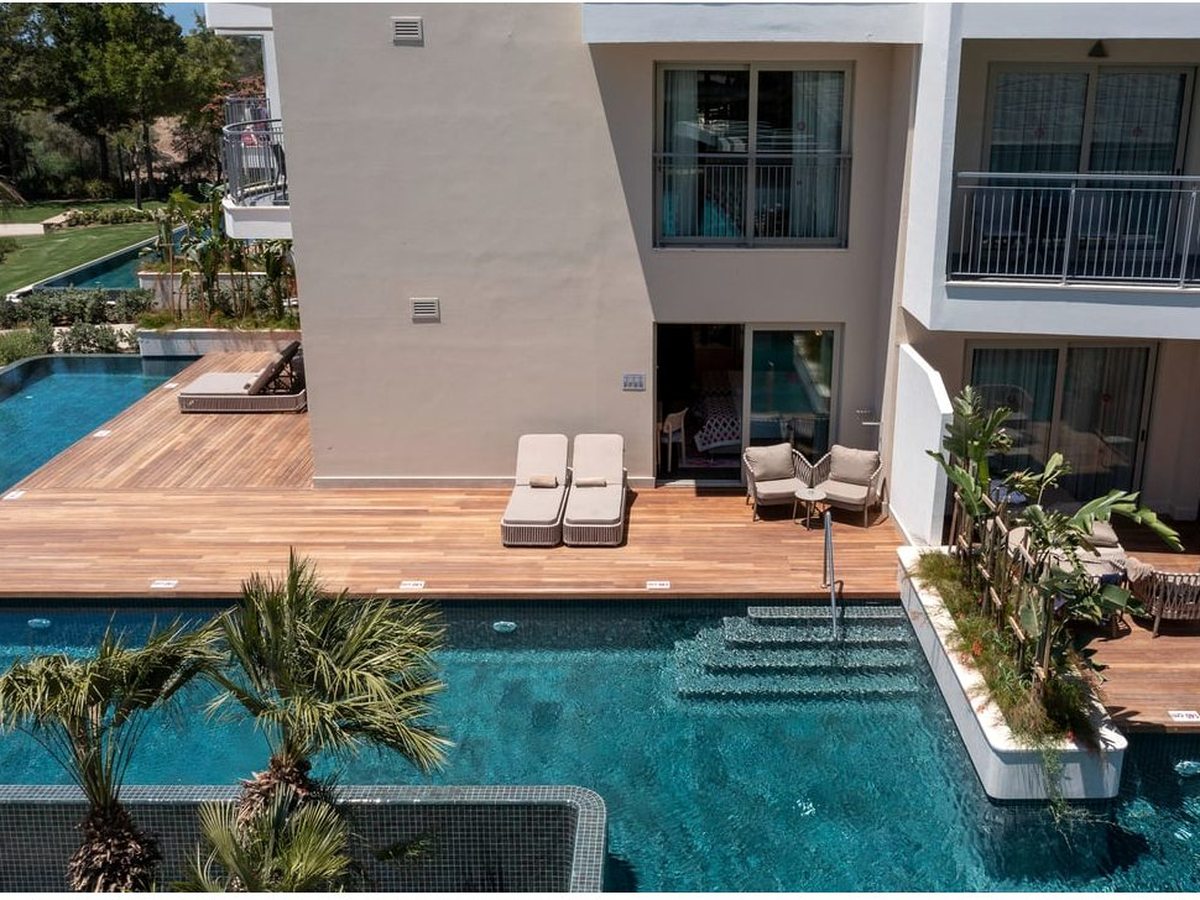 A long turquoise pool between white low-rise room blocks, with wooden decking, sun loungers and palms along the water's edge.