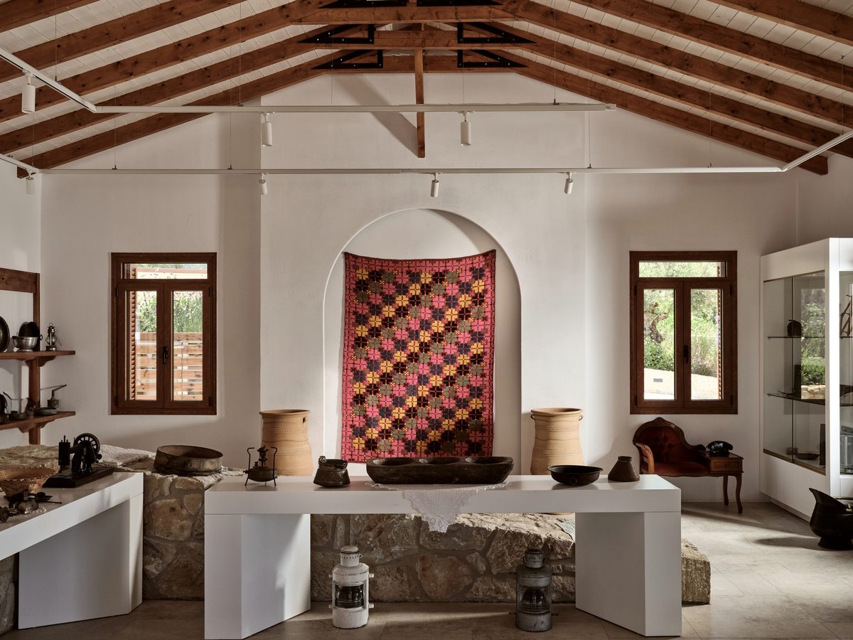 White barrel-vaulted room hung with a patchwork quilt, with old wooden and ceramic objects displayed on plinths and lanterns on a stone counter.