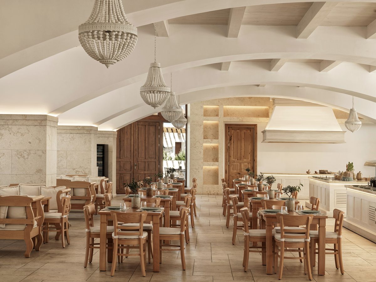 Restaurant with a white vaulted ceiling and beaded chandeliers, wooden tables and chairs, and an open kitchen counter along one side.