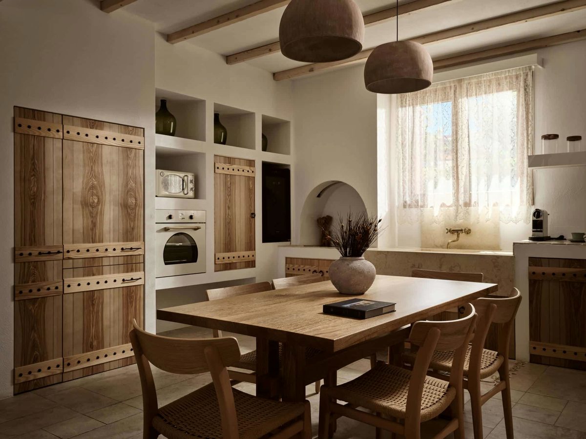 Villa kitchen and dining area with wooden cabinetry, a built-in oven and microwave, a long wooden table and cane chairs under woven pendant lights.