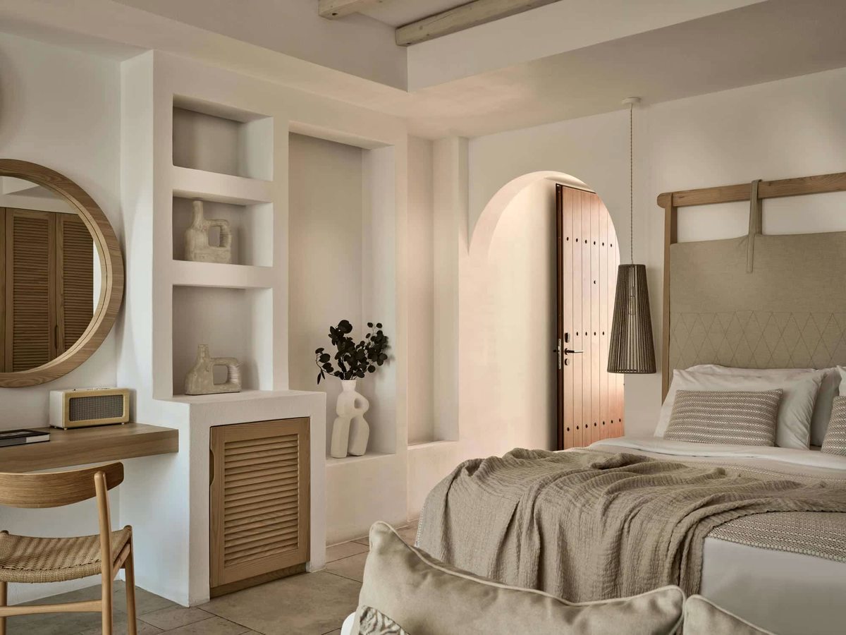 Suite bedroom with a double bed, a writing desk and round mirror, built-in plaster shelving and an arched doorway through to the bathroom.