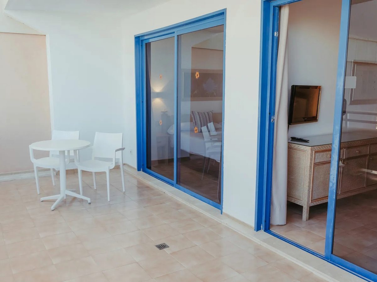 Tiled private terrace with a round white table and two chairs, blue-framed sliding doors into the bedroom and a second set into the living area.