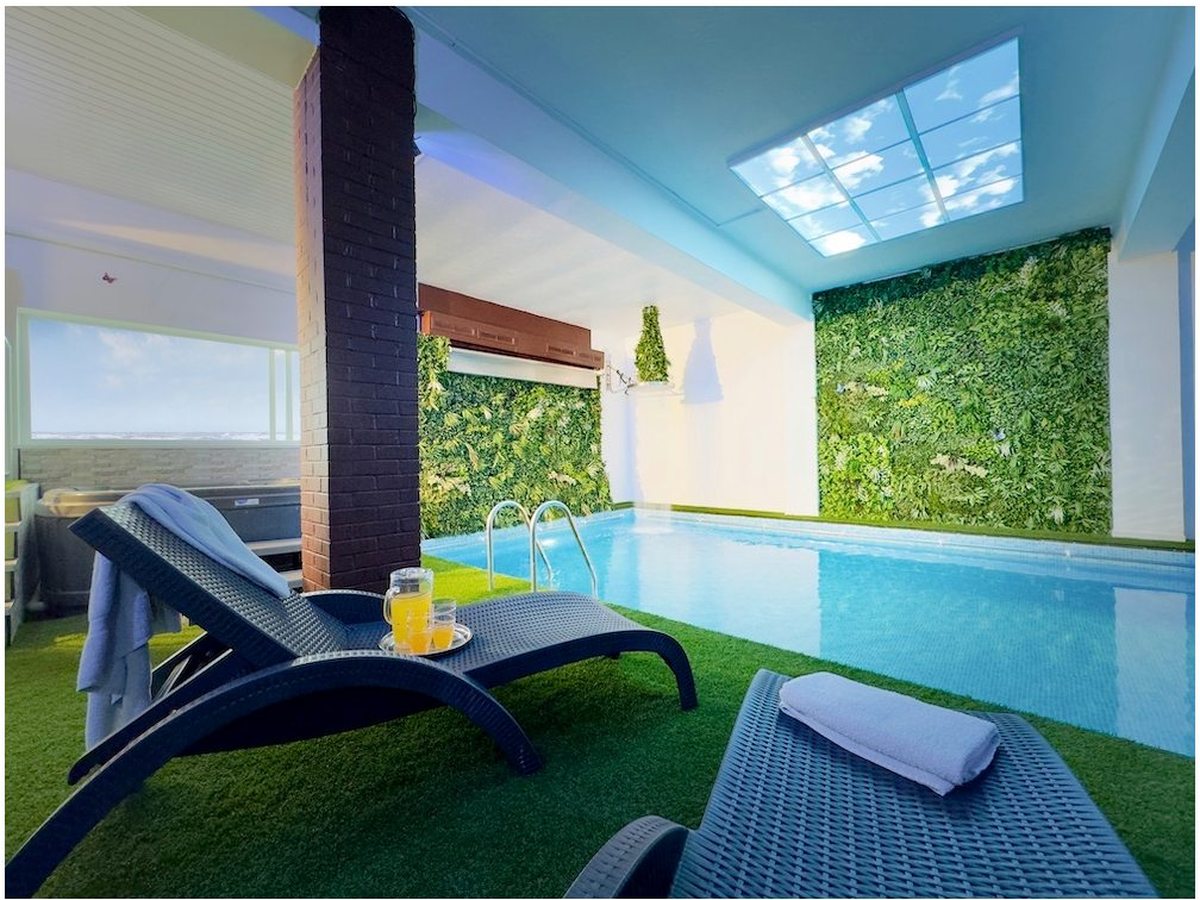 An indoor pool under skylights, with a wall of foliage, sun loungers and towels at the near end.
