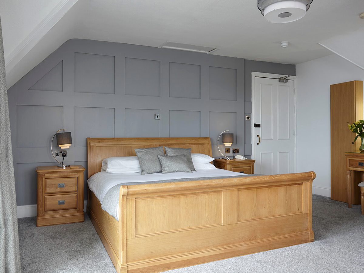 A large bedroom with an oak sleigh bed, grey panelled walls, matching bedside tables and a dressing table.