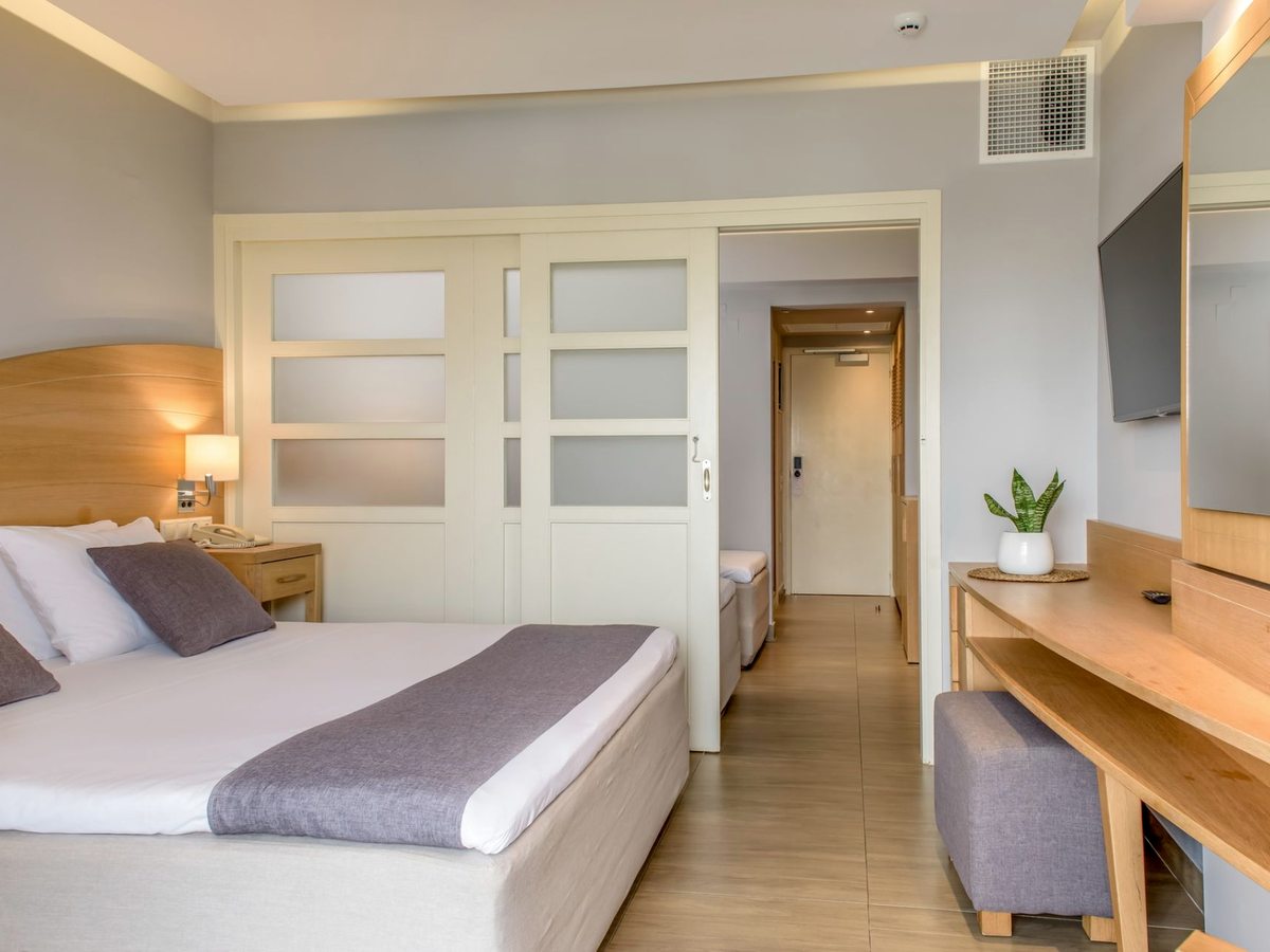 A double bed beside white frosted-glass sliding doors, open onto a second area with a single bed, with a desk and television along the wall.