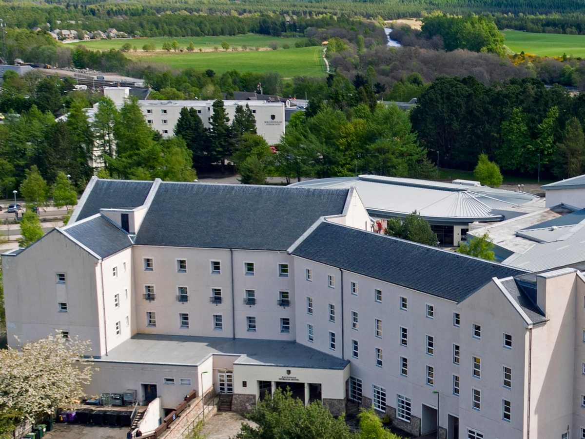 A four-storey white hotel with grey slate roofs, seen from above, with fields, the river and wooded hills stretching out behind.