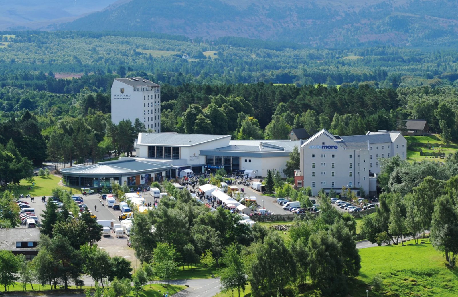 Macdonald Aviemore Resort: hotel buildings and pine woodland in the centre of Aviemore, with the Cairngorm mountains behind.