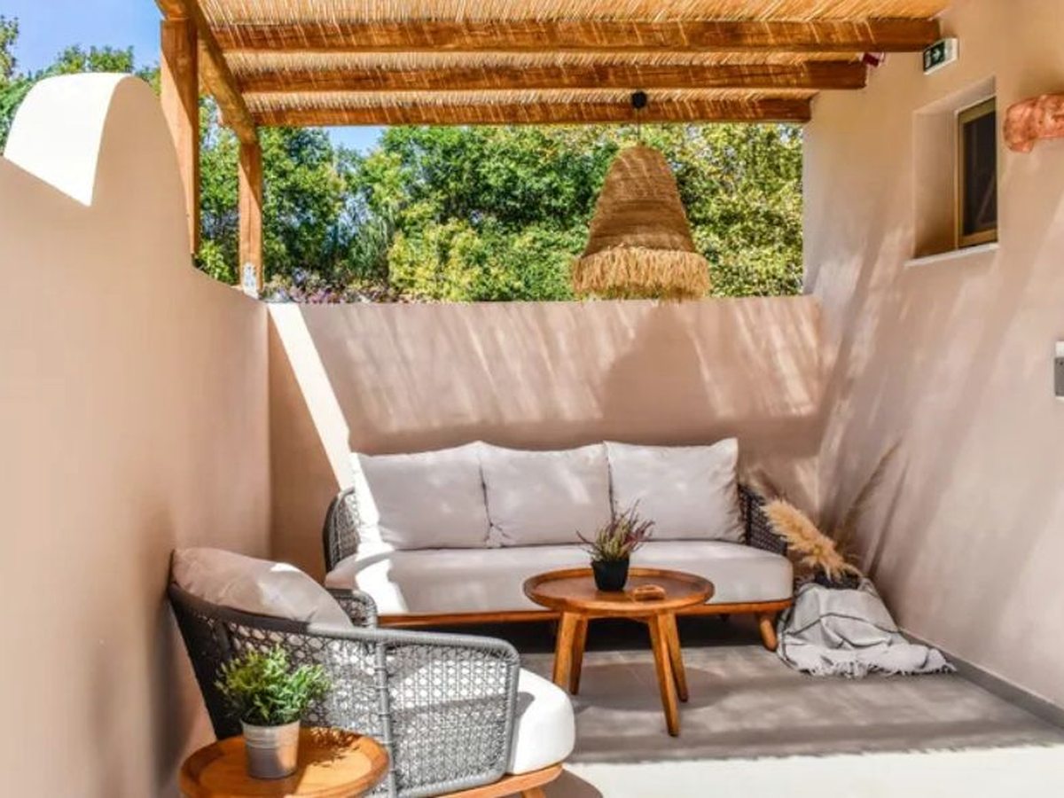 Enclosed ground-floor terrace with rendered walls, a reed-covered pergola overhead, a long cushioned sofa, a woven armchair and a round wooden coffee table.