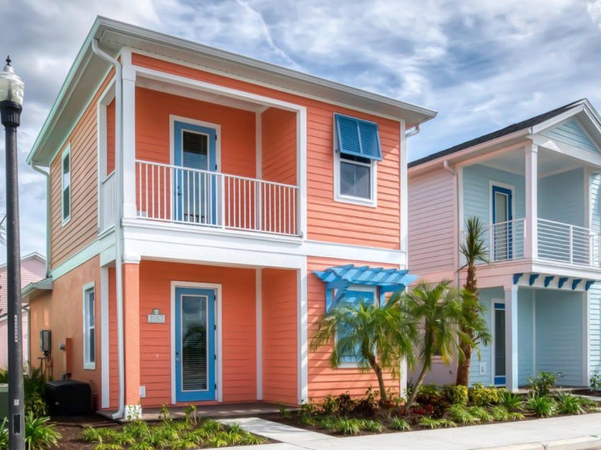 Two-storey coral and pastel cottages with covered white-railed balconies and turquoise entrance awnings, palms alongside.