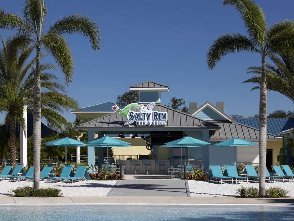 An open-air poolside bar-and-grill building with 'Salty Rim Bar & Grill' signage, turquoise parasols, loungers and palms beside a pool deck.