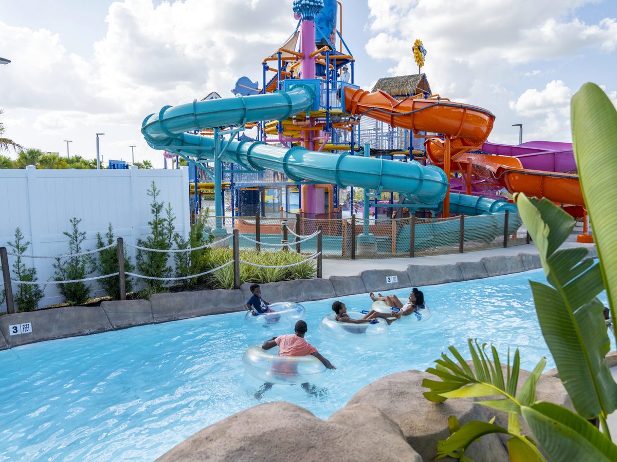A lazy river with people floating on tubes past a complex of twisting turquoise, blue, orange and purple water slides.