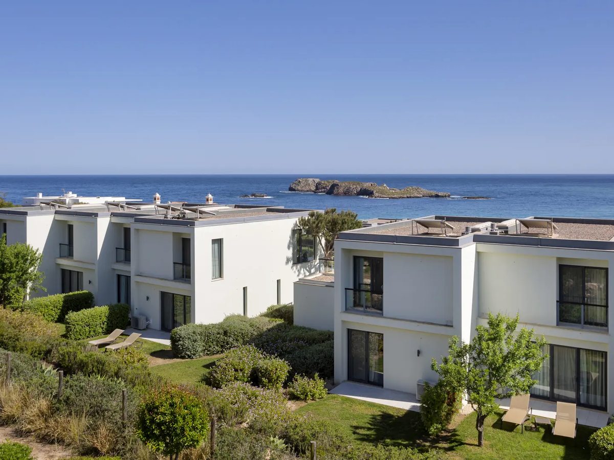 Two-storey white houses with balconies and lawned gardens, sun loungers on the grass and the deep blue Atlantic with an offshore rock behind.