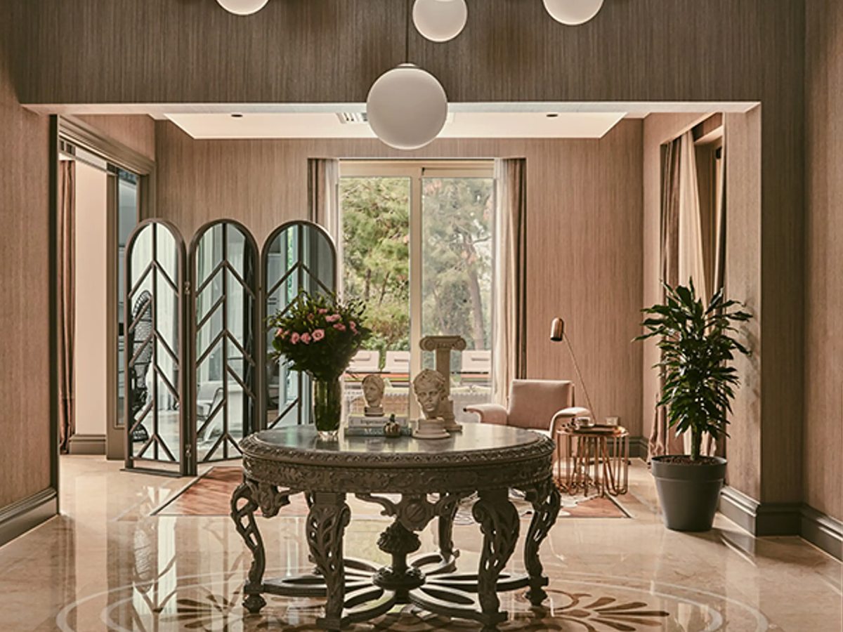 A marble-floored hall with an ornate round centre table and flower arrangement, arched folding screens and globe pendant lights.