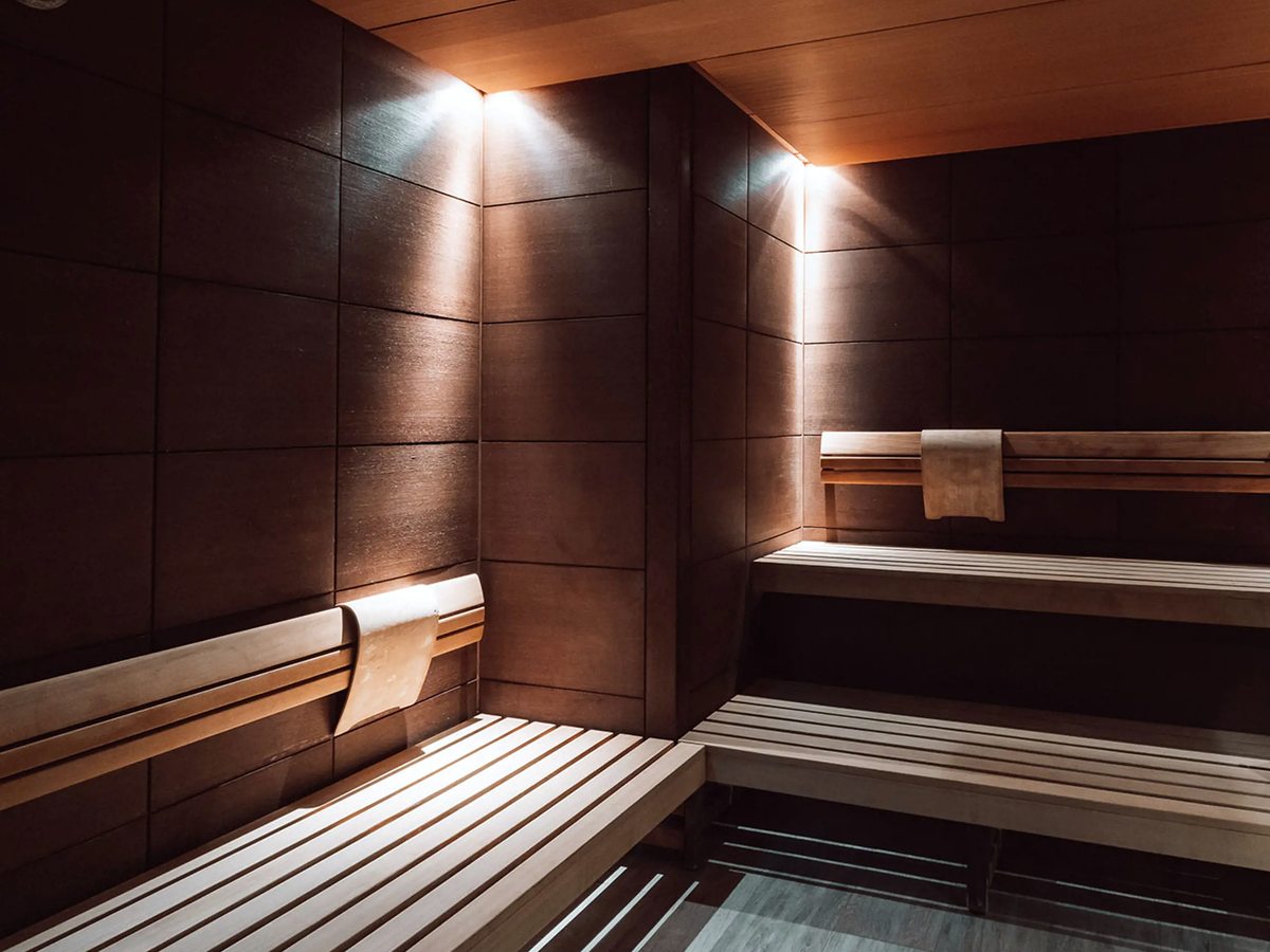 A wood-lined sauna with tiered slatted benches, a folded towel and small downlights in the ceiling.