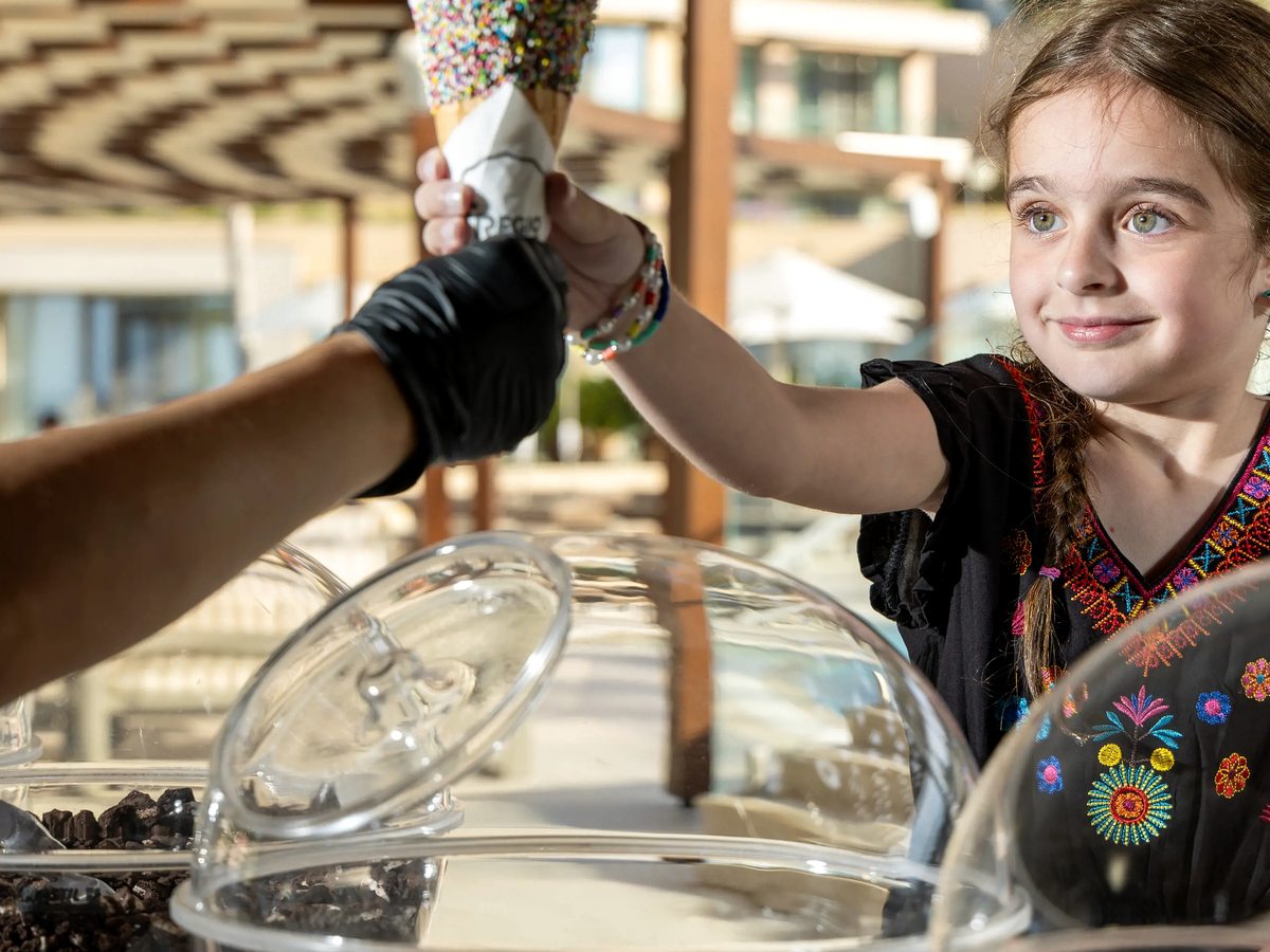 A member of staff passing a filled ice cream cone across a glass gelato cabinet to a young girl.
