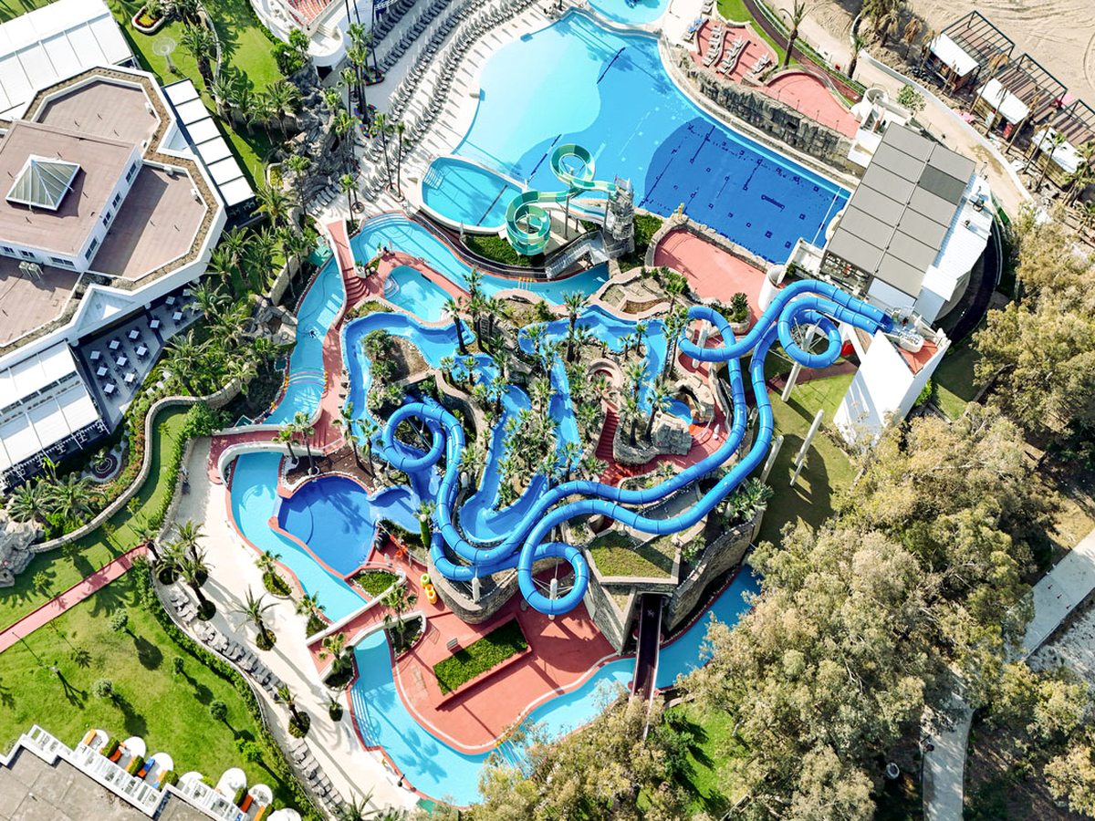 Aerial view of the water park, with blue tube slides coiling above red decking and a water channel looping around the whole structure.