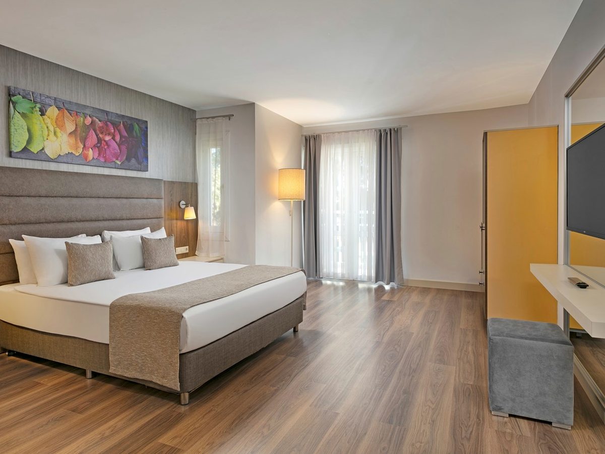 Guest room with a double bed, wood-effect floor, wall-mounted television, desk and an orange wardrobe.