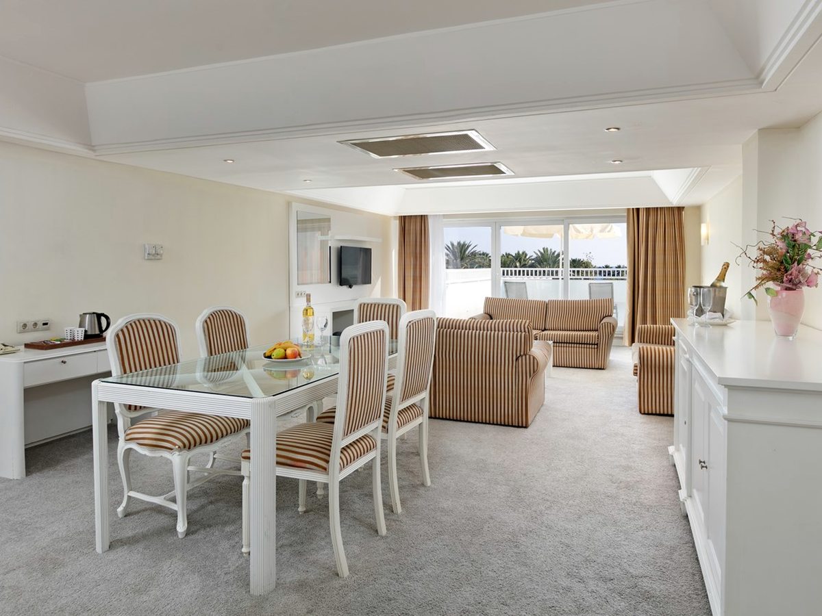Suite lounge with striped sofas and armchairs, a glass dining table and chairs, and a door out to a furnished balcony.