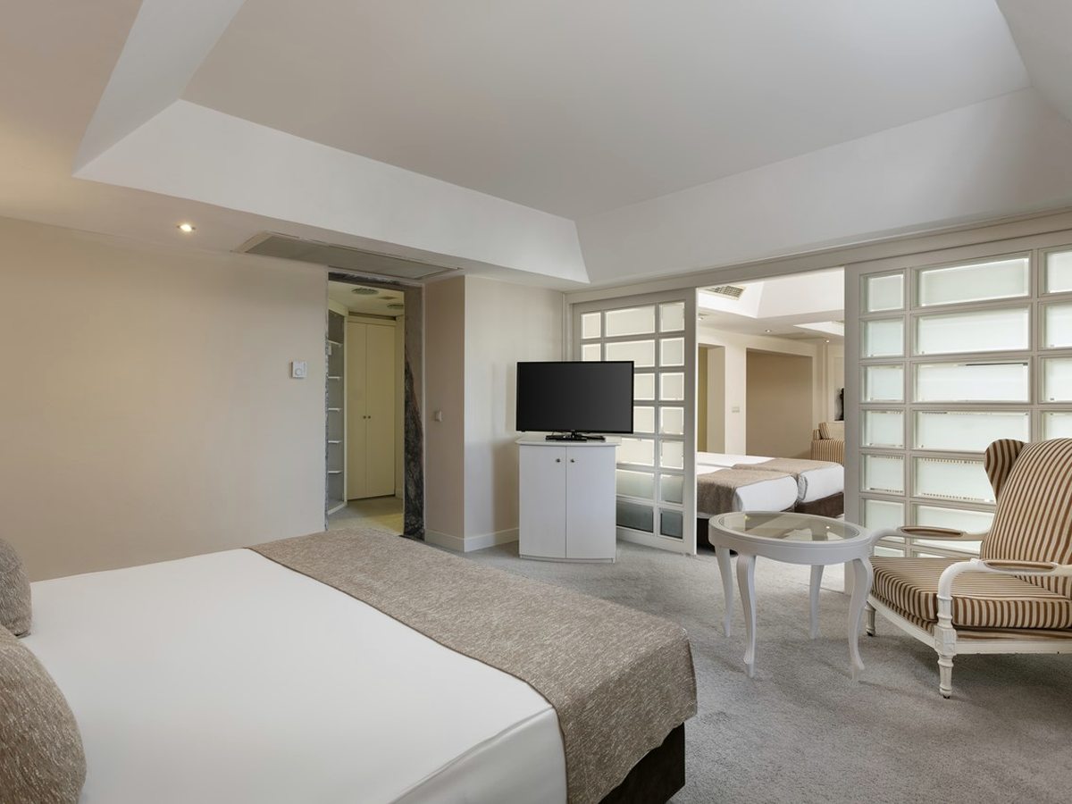 Suite bedroom with a double bed, a television on a cabinet and two striped armchairs beyond a screen partition.