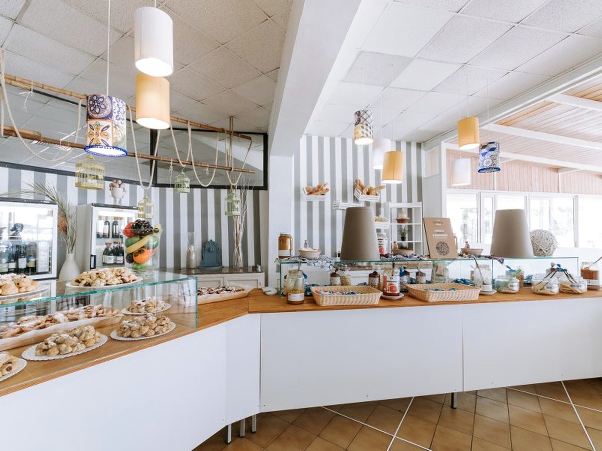 A curved buffet counter set with trays of Sicilian pastries and biscuits behind a glass screen, with bread baskets and jars along the top and pendant lights above.