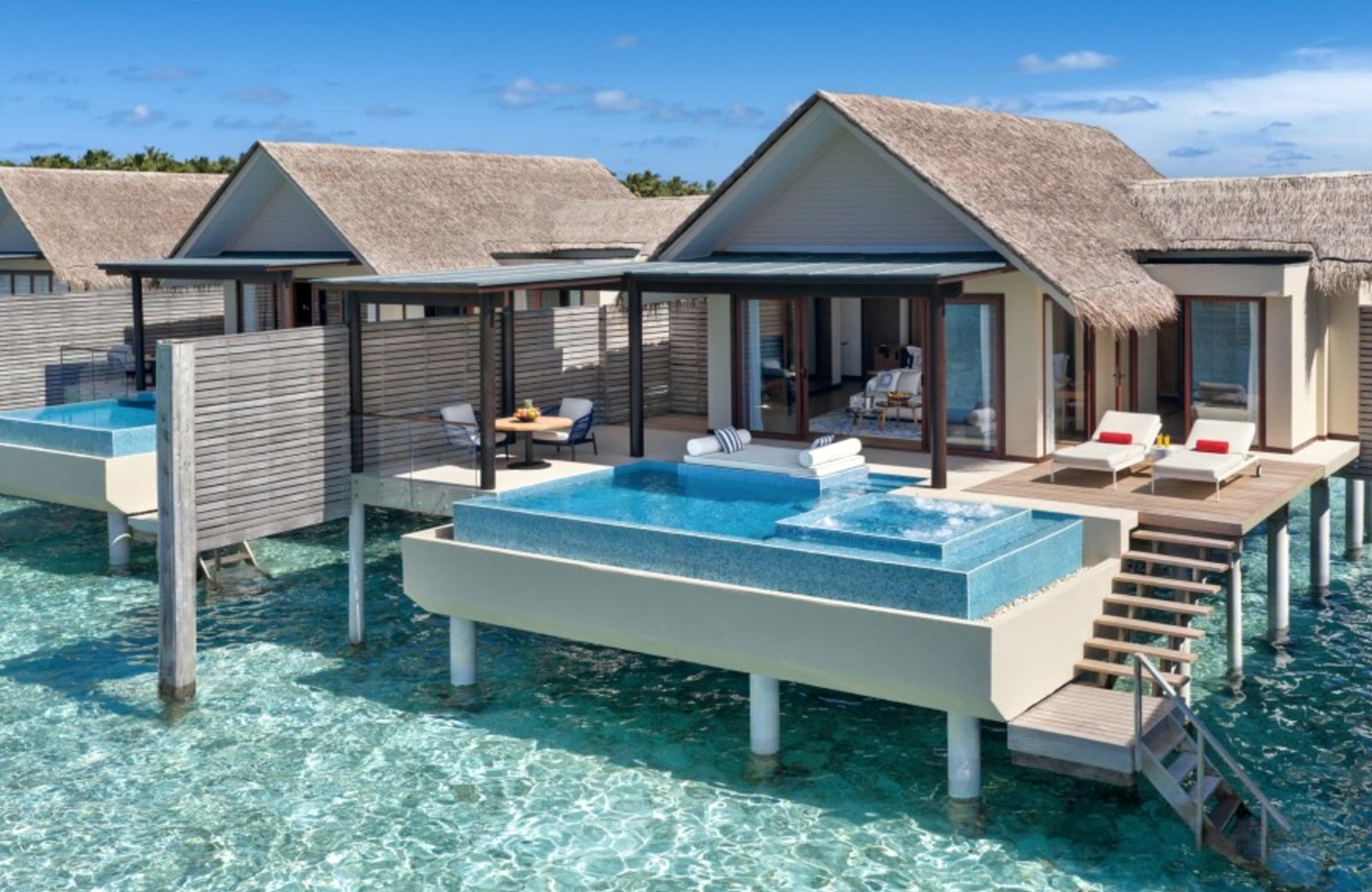 Thatched overwater villas on stilts above a clear turquoise lagoon, each with a private pool, a jacuzzi, sun loungers and timber steps down into the water.