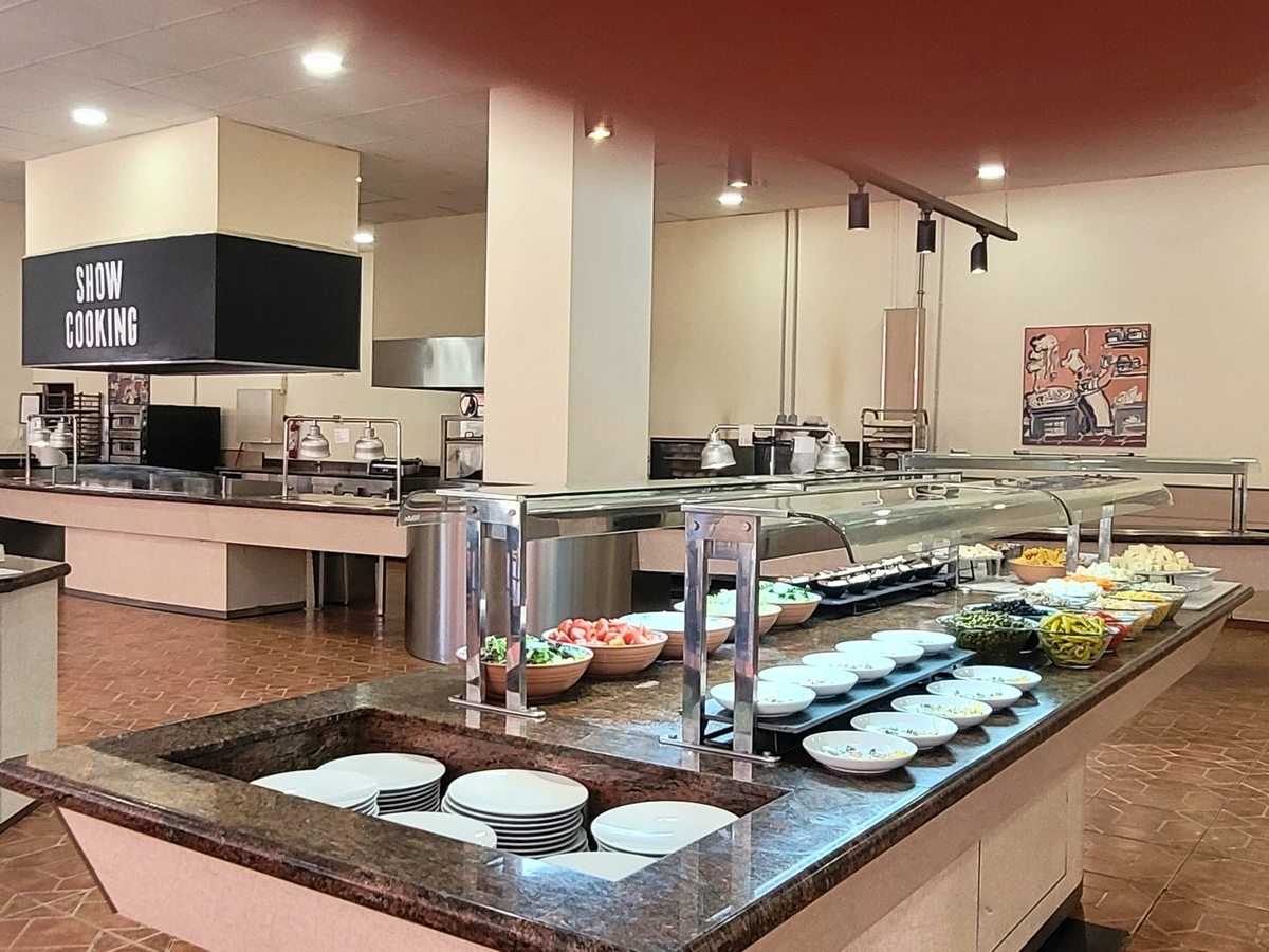 Granite-topped buffet counter with stacked plates, salad bowls and covered dishes in front of an open cooking station under an extractor hood marked Show Cooking.