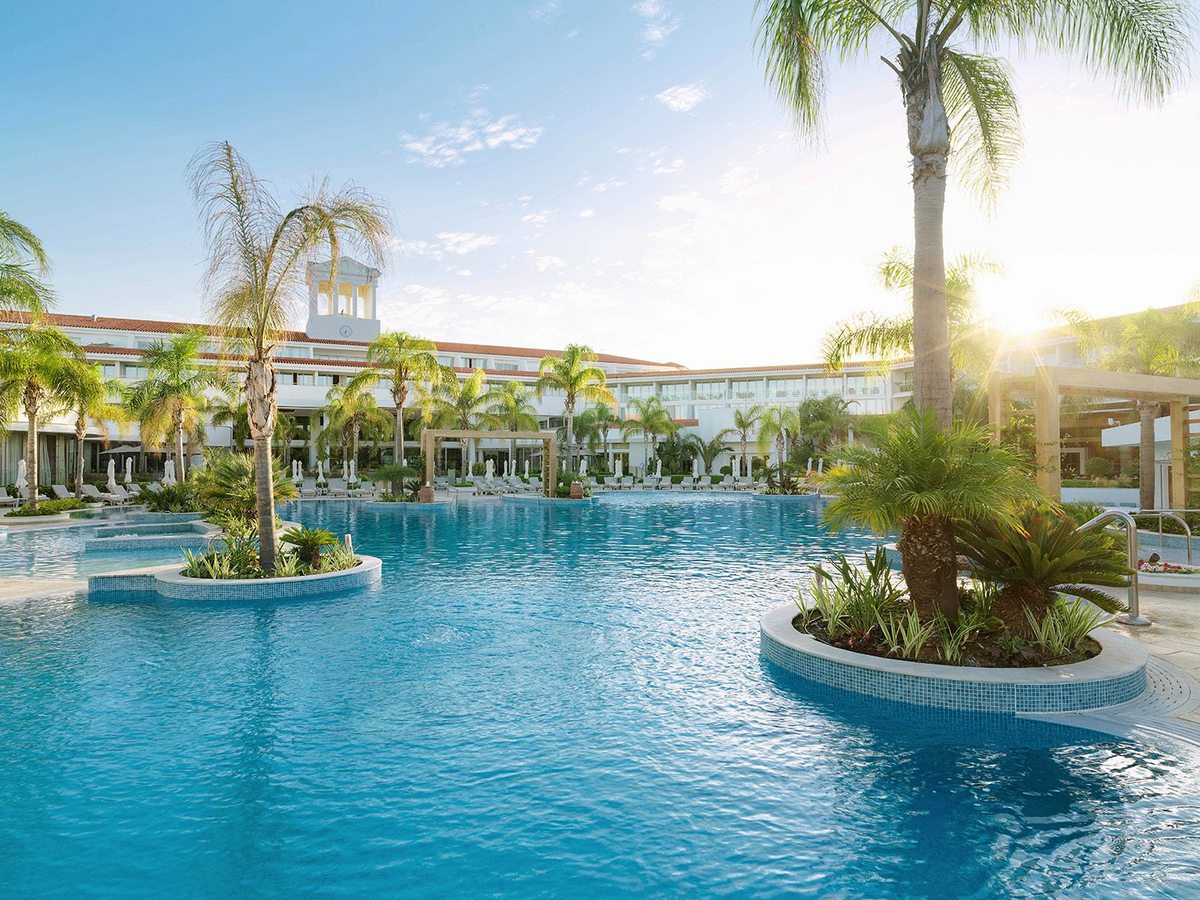 Free-form lagoon pool with planted islands of palms and cycads, the low resort buildings behind and the sun low in a clear sky.