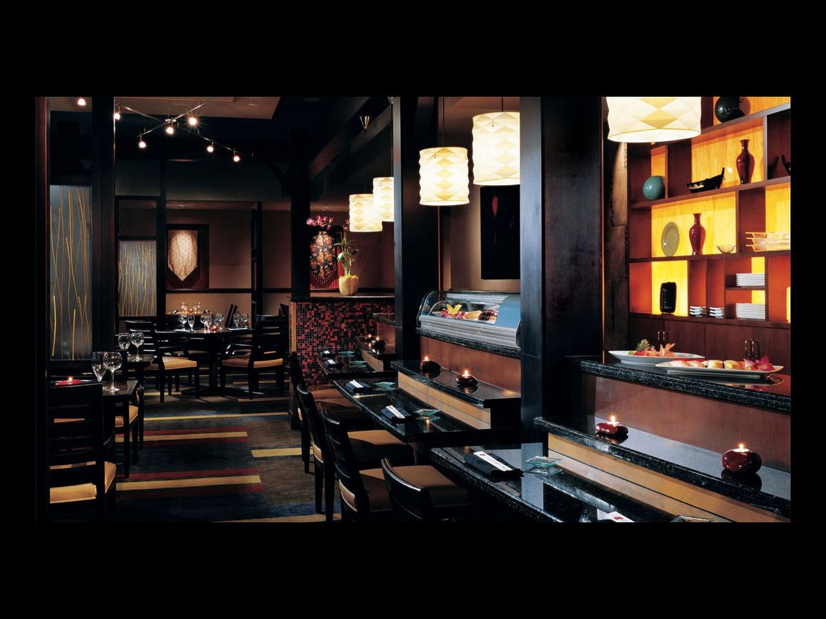 A dark-toned restaurant with set tables, black chairs, pendant lights and illuminated alcoves in red and orange.