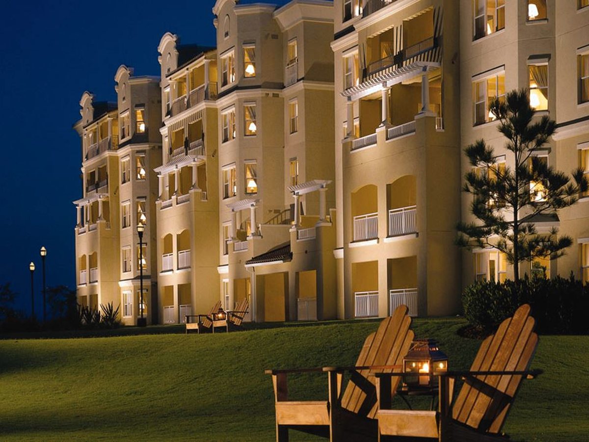 A multi-storey resort building lit at night, with an outdoor firepit and Adirondack chairs on a lawn under a dark blue sky.